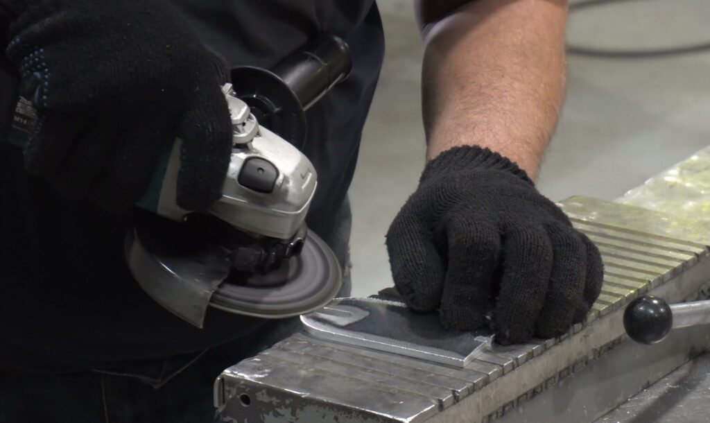 gloved hand removing burrs from metal part